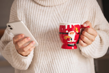 Christmas time. Closeup on woman with red santa mug in beige sweater sending text message using...