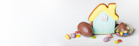 Broken Easter chocolate eggs, house shaped cookie and colorful decorations on a light background....