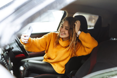 Portrait of a young casual woman in orange sweater texting on her smartphone or making video call...