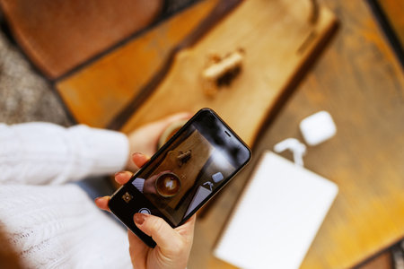 Woman hands taking a picture of a coffee cup with smart phone and laptop at a coffee shop