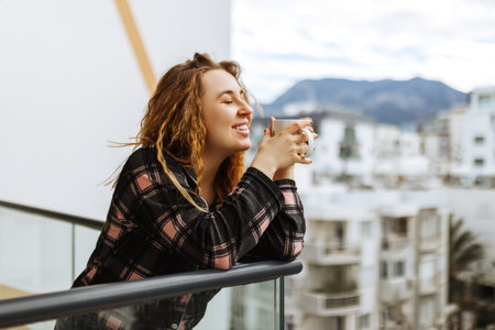A young, brunette woman dressed in sleepwear enjoys her morning coffee outdoors on the terrace under...