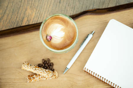 Empty notebook, white pen and cappuccino coffee on wooden table, top viewの写真素材