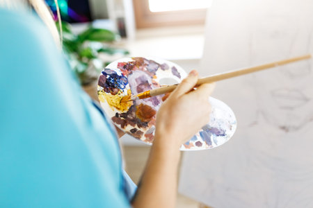 Fine art school. Closeup of artist hands holding wooden palette, mixing acrylic paint with...