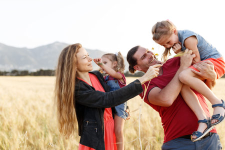 Happy family father of mother and two daughters sisters on nature at sunset.Carefree parents having fun with their kids on a fieldの写真素材