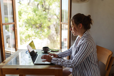 Happy young businesswoman sitting at table with laptop next to window. Skilled manager saleswoman...