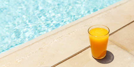 Glass of fresh cool orange juice drink on swimming pool board, summer tropical holiday conceptの写真素材