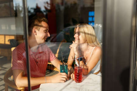 Romantic loving couple drinking lemonade, having a date in the cafe, view through windowの写真素材