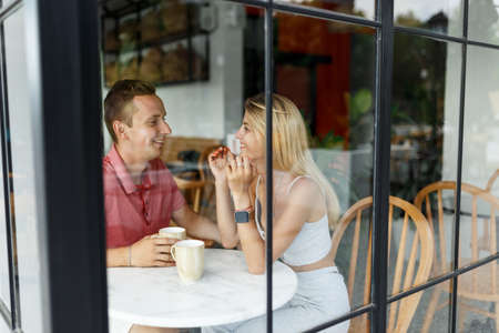 Romantic loving couple drinking coffee, having a date in the cafe, view through windowの写真素材