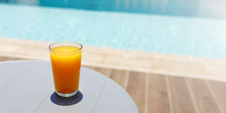 Glass of fresh cool orange juice drink on table next to swimming pool , summer tropical holiday conceptの写真素材