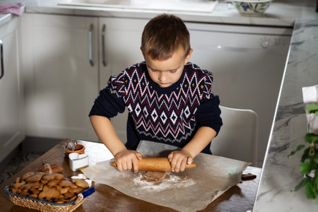 A boy prepares gingerbread cookies in the kitchen. Christmas family traditions. Leisure of the child during the New Year holidaysの写真素材