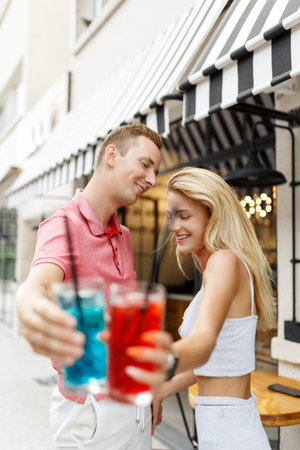 Defocused young couple in front of outdoor bar drinking cocktailsの写真素材