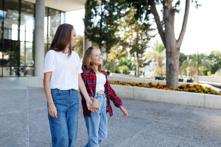 Woman walking and chatting with daughter schoolgirl after school outdoors. Cheerful teen female speaking with mother in good mood. Talk conceptの写真素材