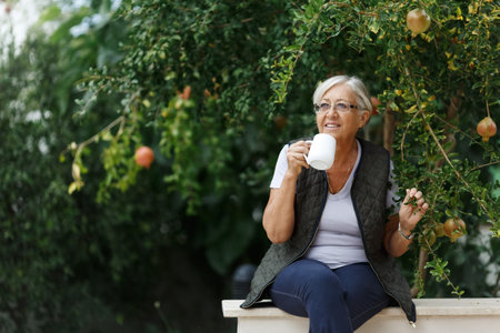 Senior grey hair woman having tea in sunny garden stunning countryside. retreat, retirement and happy senior lifestyle concept.の写真素材