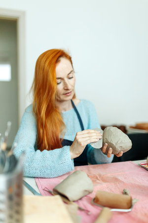 Pottery studio, artisan business,red hair female potter holding ceramic bowl ready for firing in a...