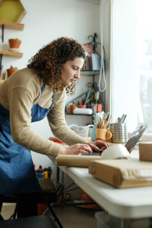 Young woman run pottery business, focused busty female entrepreneur, produce ceramic items. Small...