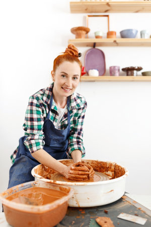 Happy female sculptor making clay pot on pottery wheelの写真素材