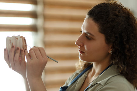 Concentrated woman painting clay jug with colorful paint shaping and sculpturing earthenware cup in...