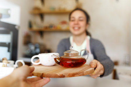 Happy young woman in apron, startup come true. Small business concept. Family business, cafe place. Giving orders, holding tea tray and cup, close up.の写真素材