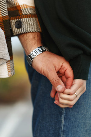 Close up couple hands touching on field over beautiful sunset. casual clothing. Man hands wear...