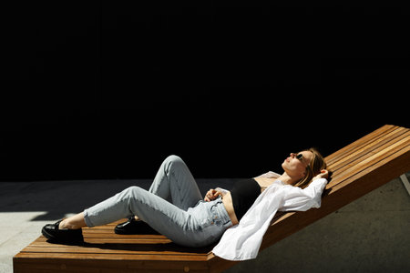 Stylish pretty woman lying on bench at city street. Woman resting at summer day outdoors. copyspace....