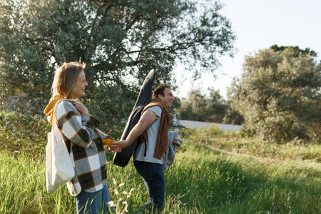 Young middle age couple walking along happily talking in the park. Mature couple in summer park. Man and woman in casual clothes with guitar and picnic bag outside in spring Cyprus nature.の写真素材