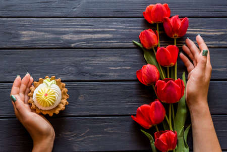 cupcake and red tulips in hands on a black wooden backgroundの写真素材