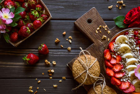 granola with fruits, berries, cookies and strawberries on a brown board on a black wooden backgroundの写真素材