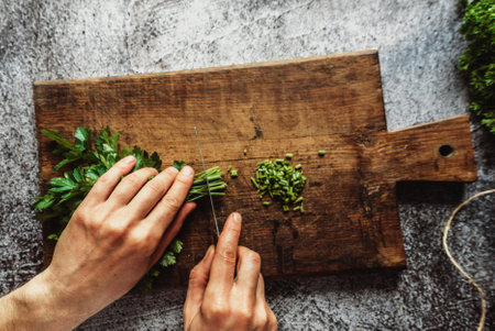 a man cuts parsley with his hands on a brown wooden board for salads or other dishesの写真素材