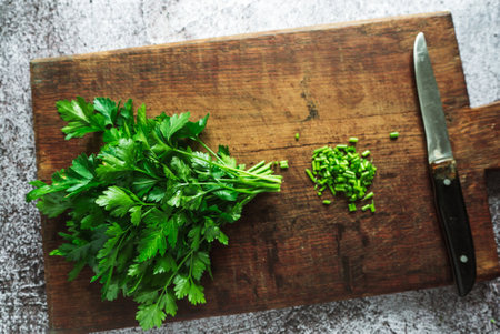 green fresh fragrant parsley with a knife for slicing greens lies on a wooden board on a gray background. top viewの写真素材