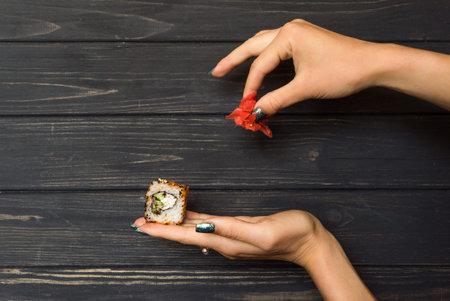 hands holding marinated ginger and sushi on a black wooden background