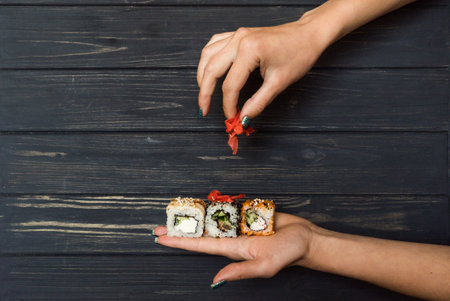 hands holding marinated ginger and sushi on a black wooden backgroundの写真素材