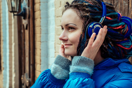 girl with dreadlocks in a blue jacket listening to music in blue headphonesの写真素材