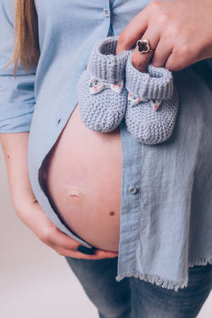 Pregnant woman in blue shirt and jeans holding baby's bootees on her bellyの写真素材