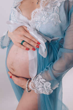 Pregnant girl in blue dress holding her belly on white background, close upの写真素材