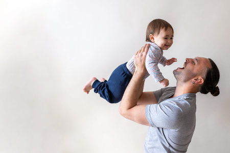 Happy father playing with little daughter raising her by his hands on Father's Day holiday