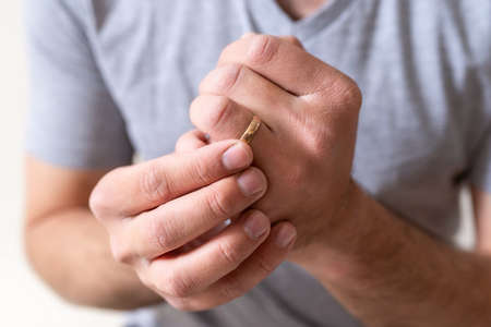 Man holding and rolling his wedding golden ring on left hand finger on white background close upの写真素材
