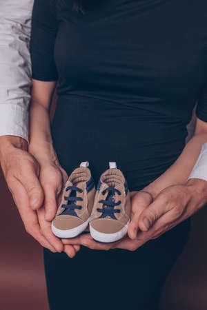 Pregnant woman and her husband holding first baby's booties close up verticalの写真素材