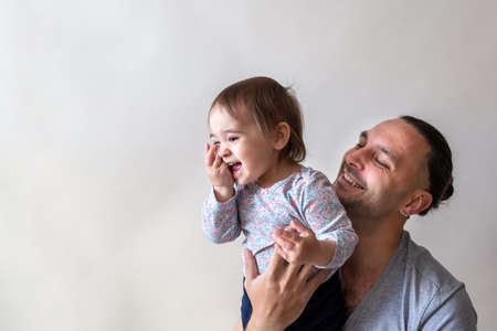 Long hair father smiling and holding his little happy daughter close up. Captured on white studio backgroundの写真素材