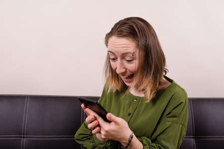 Happy woman in green dress looking on phone in hands emotionalの写真素材