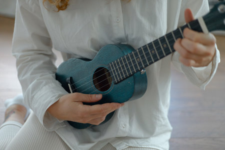 close-up of a ukulele in the hands of a girl in a white shirt.の写真素材