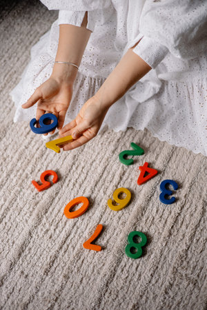 young woman holding multi-colored wooden numbers in her hands to teach children to count
