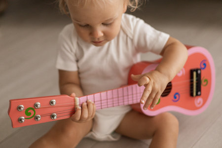 Cute blonde little baby playing on a childrens pink guitar sitting on the floor at homeの写真素材