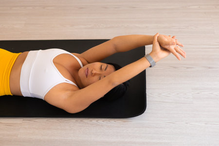 Beautiful korean tired woman in yellow and white sportswear laying on a yoga mat after fitness...