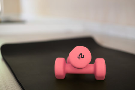 Close-up with blurred background pink dumbbells on a black mat in light beautiful sport studio,...