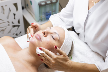 Cosmetology procedure in beauty studio. Close-up hands, applying cleanser gel on models faceの写真素材