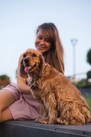 Portait of a Young beautiful woman hugs and kisses her cocker spaniel dog, lovely pet, summer sunset in public park, blurred backgroundの写真素材