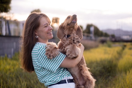 portrait of young beautiful woman and her cocker spaniel dog, summer sunset in public park