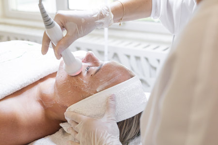 Cosmetology procedure in beauty studio. Doctor in white medical uniform doing a face procedure for...