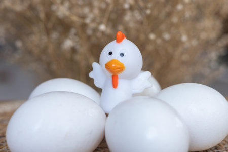 Toy chiken with white real eggs, Easter card, beige straw blurred backgroundの写真素材