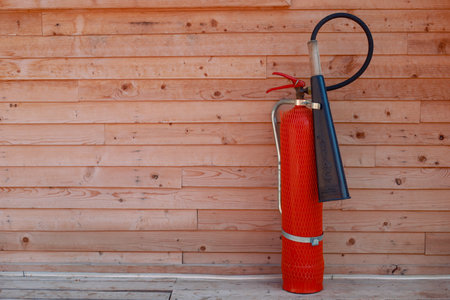 Red classic fire extinguisher stands on the floor outdoors against the background of a wooden wall. Fire safety in a wooden country houseの写真素材